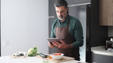 Man preparing healthy meal following online recipe on tablet