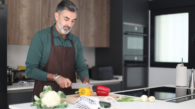 Mature man cooking fresh healthy vegetables in kitchen