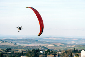 Paramotor ascending in a clear sky, offering an aerial view of green fields and distant rolling hills