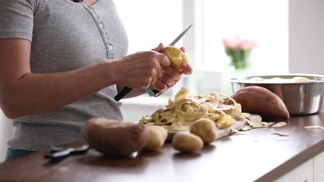 Woman Peeling Raw Potatoes And Vegetables With A Knife In The Kitchen