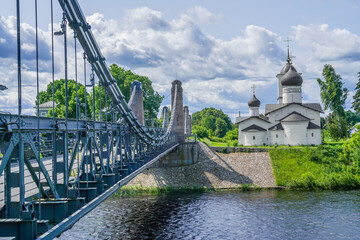 Fototapeta premium Suspension bridge over Velikaya River leading to St Nicholas the Wonderworker Church in Ostrov, Pskov oblast, Russia. stock photo 