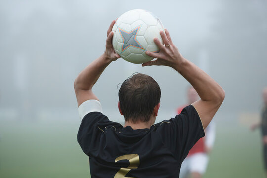 Player performs a throw-in during a soccer match in foggy weather on a grass field in the early morning