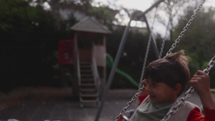 Child swinging high in air while toddler glides below creating dynamic playground moment showing motion speed, balance, and natural shared childhood play during active outdoor time in park environment