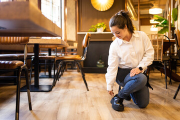A young woman between 20 and 30 years old with Down syndrome works as a waitress in a modern cafe.The girl is bent down to tie her shoelaces.Concept of trisomy 21.