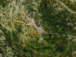 Aerial view of a path winding through the rugged terrain of Rondane, where mossy greens meet stony greys under the vast Norwegian sky, Dovre, Innlandet, Norway.