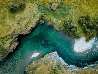 Aerial view of Rondane's teal river snaking through rugged cliffs and verdant slopes, a cabin perched on the edge, Dovre, Innlandet, Norway.