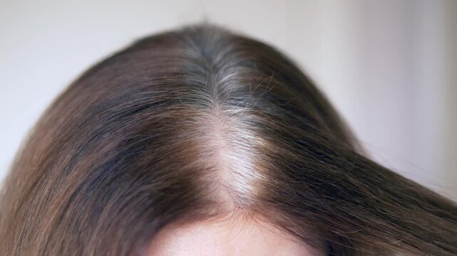 Confident woman touching gray hair at home, gently checking silver strands and caring for early gray roots with calm attention. Scene highlights confidence boosting hairstyle, natural aging. 