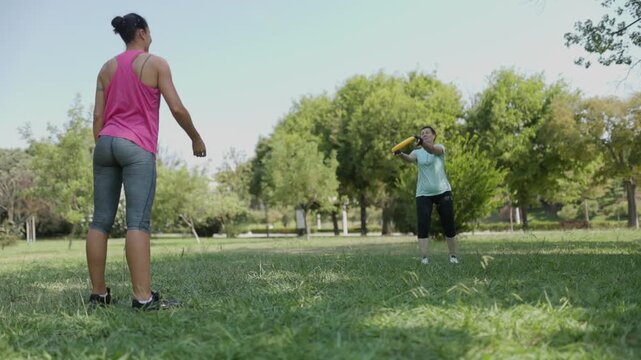 Two women playing frisbee outdoors in a summer park