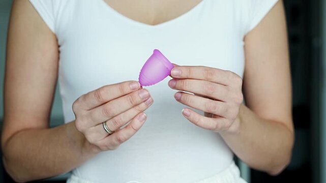 Close-up of a woman holding a pink menstrual cup in her hands, preparing for use. Promoting sustainable hygiene, personal care, and eco-friendly period products.