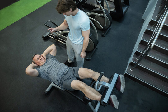 Adult man performs abdominal crunches under trainer guidance in a gym, strengthening core and improving workout technique. Senior Man Working Out in Gym