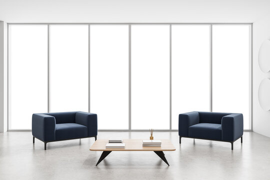 Minimalist interior scene showing two modern blue armchairs and a wooden coffee table with books, placed in front of large white background windows. 3D Rendering