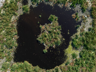 Aerial view showing a stark contrast between a natural wetland with a dark pond and a nearby landfill area.