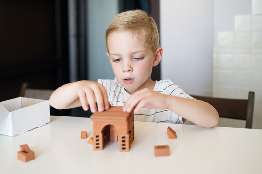 Little boy building a small brick house from an educational construction toy at the table, developing fine motor skills, problem solving and STEM learning at home.