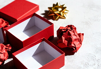 Open red gift boxes and gold bow on textured background. Empty present containers with crumpled wrapping paper flat lay