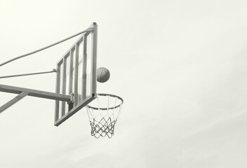Outdoor basketball hoop with a ball in mid-air approaching the net against a bright overcast sky