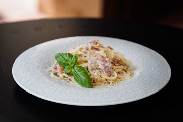 Creamy Bacon Spaghetti Carbonara With Basil Garnish On White Plate