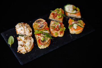 Assorted Gourmet Canapes on Black Slate Plate Surrounded by Rock Bed for Stylish Appetizer Spread