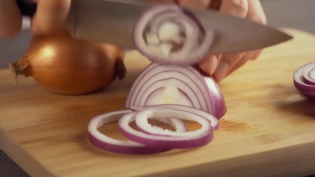 Close-up of a person's hands slicing a red onion into rings on a wooden cutting board, preparing for cooking