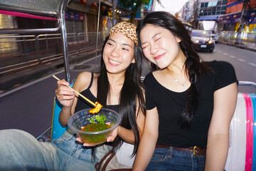 Two young woman sisters sitting tuk tuk taxi local tour hanging out trip gen Z hipster travel in Bangkok, Thailand