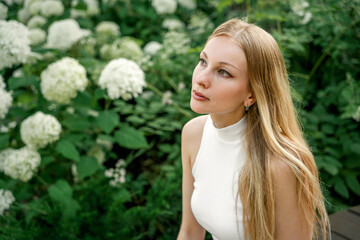 beautiful blonde woman is sitting in a city park with hydrangeas