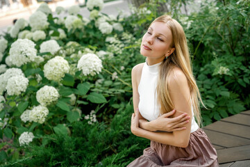 beautiful blonde woman is sitting in a city park with hydrangeas