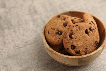 Delicious chocolate chip cookies in bowl on gray textured table, closeup