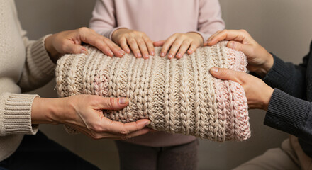 Three hands holding a cozy crochet blanket in a warm setting  