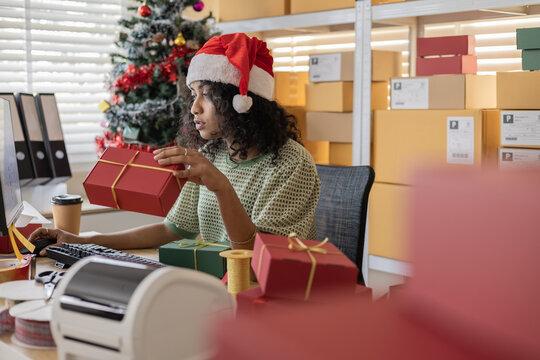 Small business holiday warehouse process showing a worker hold Christmas gifts, checking orders, arranging parcels, managing stock accuracy and coordinating ecommerce busy shipping for festive season