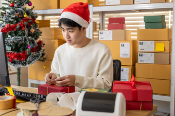 Small business warehouse working moment with new-gen owner preparing Christmas gifts, tying ribbon, organizing parcels, and managing seasonal ecommerce orders during busy holiday shipping schedule