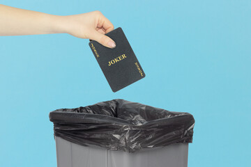 Throwing black playing card joker into the trash can, outstretched hand with playing card in front of trash can