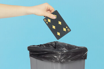 Throwing black playing card diamonds 6 into the trash can, outstretched hand with playing card in front of trash can
