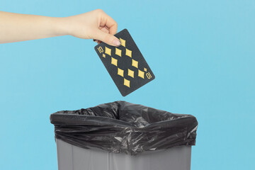 Throwing black playing card diamonds 10 into the trash can, outstretched hand with playing card in front of trash can