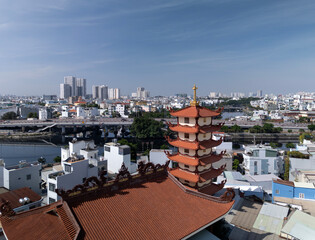 Drone view over Buddhist pagoda in busy urban area of Ho Chi Minh City, Vietnam on a sunny clear day featuring roof decoration and the transportation infrastructure of main roads and canals
