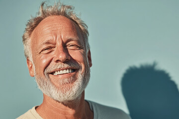 Happy senior man with a white beard smiling broadly against a blue background. portrait captures a joyful older man with a genuine smile, radiating warmth and contentment.