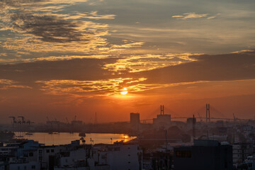 Saigon River Sunrise looking toward port and Phu My Bridge with shipping on the water and beautiful red sky.