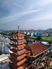 Vertical wide drone view over Buddhist pagoda in busy urban area of Ho Chi Minh City, Vietnam on a sunny clear day featuring roof decoration and the transportation infrastructure
