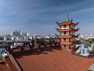 Drone view over Buddhist pagoda rooftop in busy urban area of Ho Chi Minh City, Vietnam on a sunny clear day featuring roof decoration and the transportation infrastructure of main roads and canals
