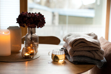 Home interior decor in brown colors: glass vase with dried flowers, candles and cup of warm tea