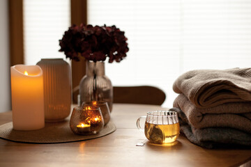 Home interior decor in brown colors: glass vase with dried flowers, candles and cup of warm tea