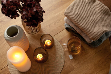 Home interior decor in brown colors: glass vase with dried flowers, candles and cup of warm tea