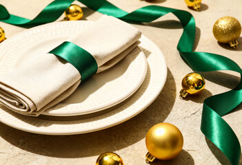 Christmas table setting with beige napkin and green ribbon on plates. Festive holiday dinner decoration with gold baubles. Elegant flat lay background
