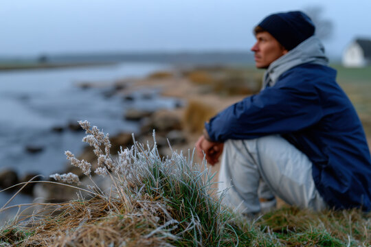 A contemplative fisherman sits by a frosty riverbank at dawn, capturing the stillness of early morning while surrounded by nature's serene beauty.