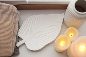 Pile of beige knitted sweaters, wooden tray, candles and vase over white background top view