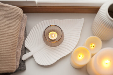 Pile of beige knitted sweaters, wooden tray, candles and vase over white background top view