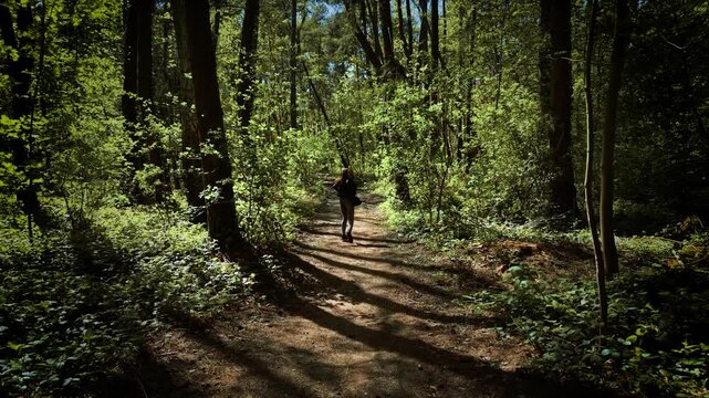 Frightened woman running through forest and looking back in fear. Scared female fleeing along woodland trail and glancing behind in panic. Terrified lady escaping from danger and turning head while