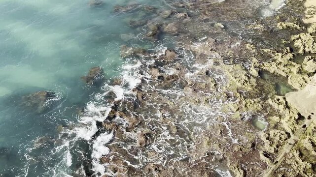 Ocean waves rolling to the rocky shore. Beautiful seascape. Aerial top view of the beautiful ocean rocky shore with rolling waves. Drone is hovering over rolling ocean waves to rocky shore