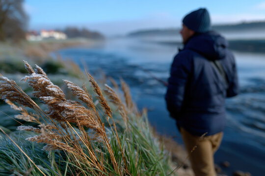 A picturesque winter scene showcasing frosted reeds swaying gently by a quiet riverbank, channeling serene vibes and the beauty of the tranquil early morning landscape.