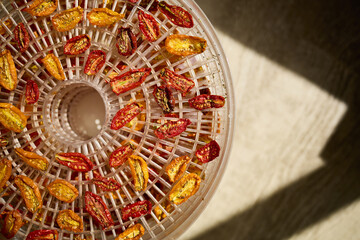 Bright red and yellow cherry tomatoes are arranged in a dehydrator, drying under warm air. This healthy method preserves their flavor, perfect for summer snacks.