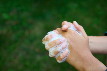 Two hands are rubbing together with soap bubbles while standing outdoors in a green garden. This activity showcases the importance of hygiene and cleanliness.