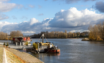 Fototapeta premium view of the Loire river along Quai du Chatelet in Orleans, France, during autumn. The paved promenade is lined under a dramatic cloudy sky with moored houseboats